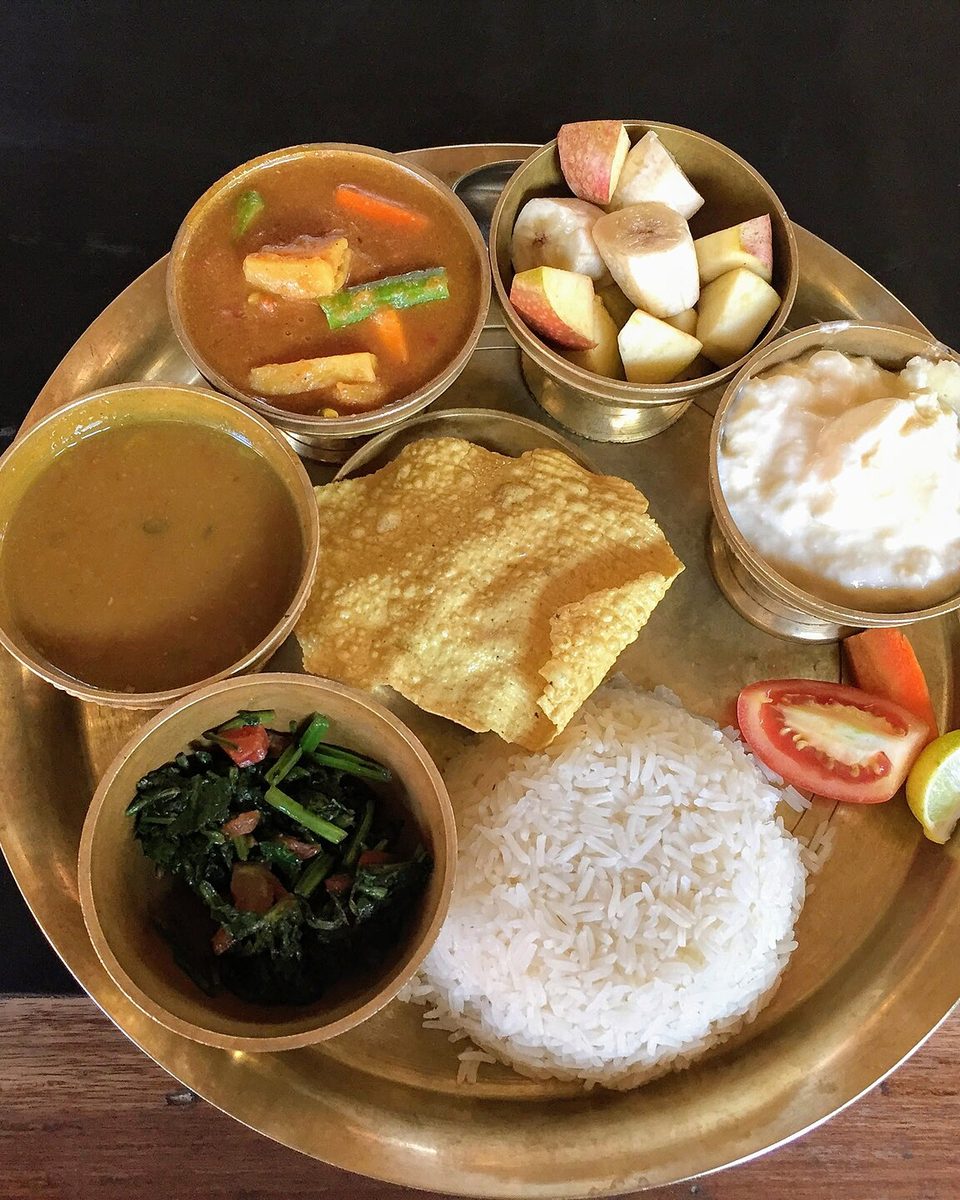 Dal bhat with lentils, rice, greens and curry on a brass plate
